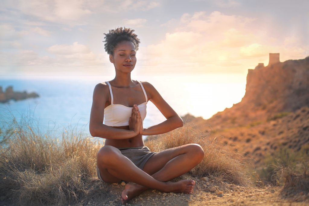 Beautiful woman doing yoga on a cliff. Behind her is an amazing sunrise landscape.